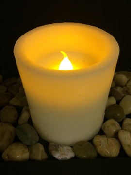 Votive candle on bed of stones, burning with a small flame in the dark